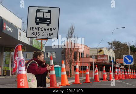 Tauranga Neuseeland - Juli 31 2023; Straßenkonen dominieren die Landschaft, während eine Frau auf dem Bordstein unter einem temporären Busschild sitzt und raucht und mobil aussieht Stockfoto