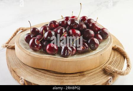 Gehobene Eleganz, frische Kirschen auf Holzständer und Beton. Summer's Bounty, saftige Kirschen auf Holz stehen auf Beton Stockfoto
