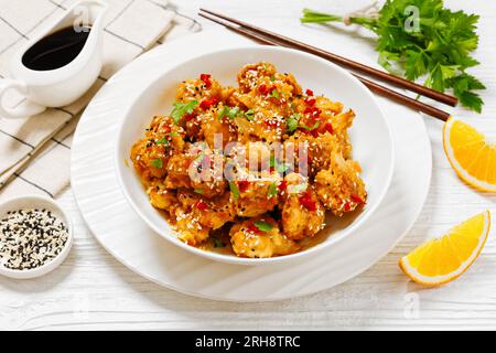 Knusprige Blumenkohlblüten mit Sesamsamen, Chiliflocken und Petersilie in einer weißen Schüssel auf einem weißen Holztisch mit Zutaten Stockfoto