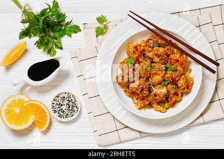 Knusprige Blumenkohlblüten mit Sesamsamen, Chiliflocken und Petersilie in weißer Schüssel auf weißem Holztisch mit Zutaten und Koteletts Stockfoto