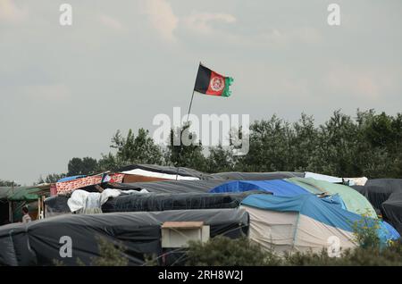 Aktenfoto vom 31.07/15. Die Flagge Afghanistans fliegt über Zelten innerhalb des Migrantenlagers, bekannt als der neue Dschungel in Calais, Frankreich. Ein afghanischer Vater, der im Vereinigten Königreich lebt, hat den "katastrophalen" Tag beschrieben, an dem die Taliban die Kontrolle über sein Land übernahmen und ihn zwangen, mit seiner Frau und fünf Kindern zu fliehen. Eid Mohammad Sultani, der sich am 15 2021. August in Kabul befand, als die Gruppe die Hauptstadt eroberte, erinnerte sich an das Geschrei inmitten des Chaos eines Tages, an den er schwer nachzudenken hat. Ausgabedatum: Dienstag, 15. August 2023. Stockfoto