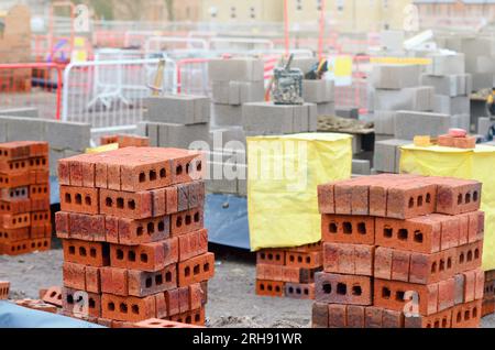 Rote Steine und Betonblöcke, die auf der Baustelle geliefert und neben dem Arbeitsort für Maurer aufgestellt wurden Stockfoto