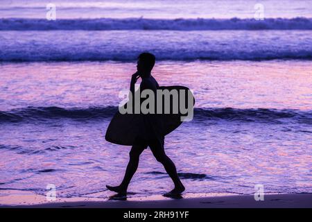 Silhouette von Surfern, die ihr Surfbrett am Sunset Beach mit lila Vibes tragen Stockfoto