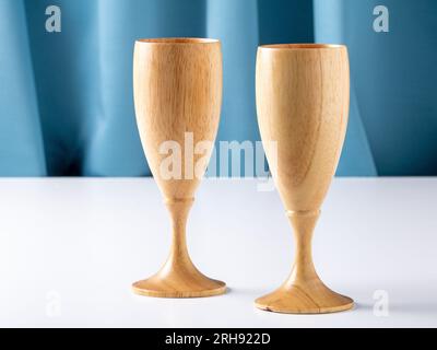 Zwei hölzerne Weingläser auf einem weißen Tisch vor einem blauen Seidenvorhang Stockfoto