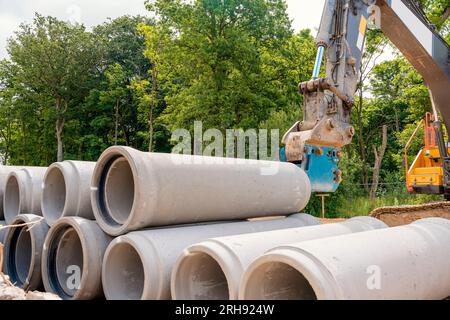 Betonrohre mit großem Durchmesser für Entwässerungsarbeiten, die auf der Baustelle geliefert und vom Bagger entladen werden Stockfoto