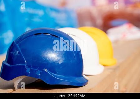 Drei Helme in verschiedenen Farben auf dem Holzbrett Nahaufnahme mit selektivem Fokus. Tragen Sie beim Bau immer persönliche und sichere Schutzausrüstung Stockfoto