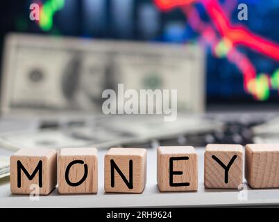 GELD das Wort auf Holzwürfeln, Würfel stehen auf einer reflektierenden Oberfläche, im Hintergrund ist ein Geschäftsdiagramm. Geschäfts- und Finanzkonzept Stockfoto