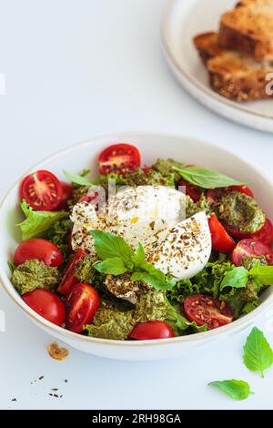Burrata-Salat mit Kirschtomaten, Pesto und Gewürzen in einer Schüssel auf weißem Hintergrund, Nahaufnahme. Stockfoto