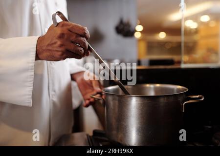 Zugeschnittene Abbildung: Koch, der Suppe aus einem großen Topf in Teller steckt Stockfoto