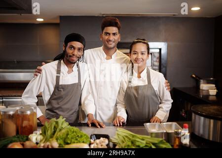 Porträt des stolzen Restaurantkochs und seines Teams, das mit frischen Zutaten am Tisch steht Stockfoto