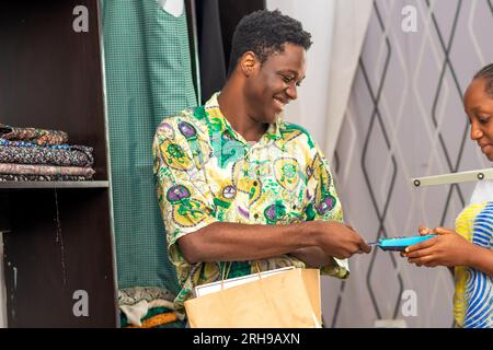 Mann, der die volle Einkaufstasche hält und die Zahlung mit Kreditkarte, POS-Terminal, durchführt Stockfoto