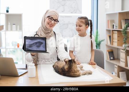Vet mit MRT auf Tablet und Mädchen posiert in der Nähe des Schreibtisches mit Katze Stockfoto