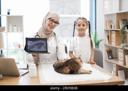 Vet mit MRT auf Tablet und Mädchen posiert in der Nähe des Schreibtisches mit Katze Stockfoto