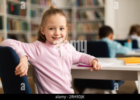 Porträt einer hübschen Schülerin, sitzt am Schreibtisch im Klassenzimmer, dreht sich um und lächelt vor der Kamera, freier Platz Stockfoto