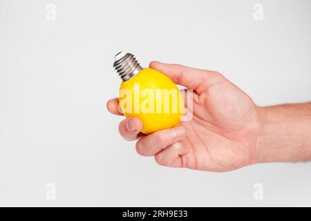 Frische Zitrone als Glühbirne in der Hand auf weißem Hintergrund. Kreatives Konzept. ECO-Energie-Idee. Abstrakte, trendige Aussicht Stockfoto