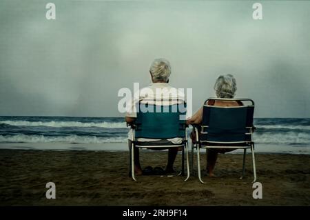 Glücklich bis ans Lebensende. Romantische Großeltern am Strand verliebt. Zwei ältere Leute sitzen am Strand nebeneinander und genießen einen bewölkten Tag. Stockfoto