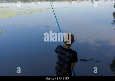 Der Teenager steht mit dem Rücken zur Stange und wartet auf ein Knabbern. Sportfischen auf dem Fluss im Sommer. Stockfoto