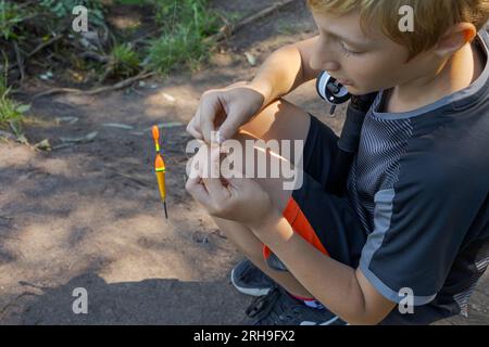 Ein Teenager richtet einen Köder ein, um Fische zu fangen. Sportfischen auf dem Fluss im Sommer. Stockfoto