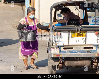 SAMUT PRAKAN, THAILAND, FEBRUAR 02 2023, eine ältere Frau in einer Schürze, ein motorisiertes dreirädriges Tuk Tuk Taxi Stockfoto