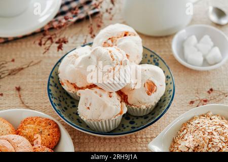 Nahaufnahme von Merengues almendrados, spanisch gebackenen Baiser mit Mandeln, in einer weißen Keramikschüssel auf einem Tisch mit brauner Tischdecke neben einem Stockfoto