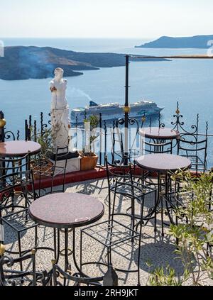 Blick auf das Meer und das Kreuzfahrtschiff von der Terrasse mit Stühlen und Tisch, Fira, Santorin, Griechenland Stockfoto