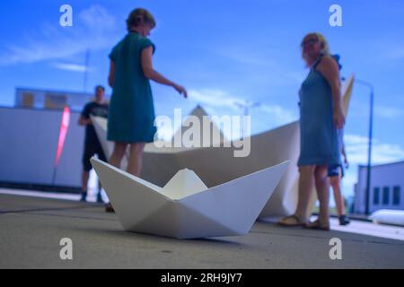 Marienborn, Deutschland. 15. Aug. 2023. Teilnehmer der Aktion „100 Boote - 100 Millionen Menschen“ falten ein XXL-Papierboot am German Division Memorial Marienborn. Die Papierbootfaltung war der Anstoß für ein deutschlandweites sozial kritisches Kunstprojekt der AWO Volunteer Academy Sachsen-Anhalt. Insgesamt müssen 100 XXL-Papierboote an verschiedenen Stellen gefaltet werden. Die Kunstwerke werden in Berlin zum Weltflüchtlingstag am 20. Juni 2024 aufgestellt. Kredit: Klaus-Dietmar Gabbert/dpa/Alamy Live News Stockfoto