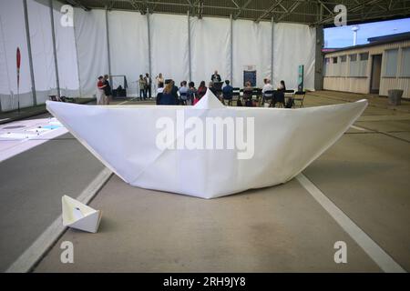 Marienborn, Deutschland. 15. Aug. 2023. Ein großer und ein kleiner Papierbootstand unter einem Dach der Gedenkstätte für die Deutsche Division Marienborn. Dort hatten die Teilnehmer der Aktion "100 Boote - 100 Millionen Menschen" riesige Papierboote gefaltet. Die Faltung von Papierbooten war der Beginn eines sozialkritischen deutschen Kunstprojekts der AWO Volunteer Academy Sachsen-Anhalt. Insgesamt müssen 100 große Papierboote an verschiedenen Stellen gefaltet werden. Die Kunstwerke werden in Berlin zum Weltflüchtlingstag am 20. Juni 2024 errichtet. Kredit: Klaus-Dietmar Gabbert/dpa/Alamy Live News Stockfoto