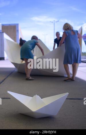 Marienborn, Deutschland. 15. Aug. 2023. Teilnehmer der Aktion „100 Boote - 100 Millionen Menschen“ falten ein riesiges Papierboot am German Division Memorial Marienborn. Die Papierbootfaltung war der Anstoß für ein deutschlandweites sozial kritisches Kunstprojekt der AWO Volunteer Academy Sachsen-Anhalt. Insgesamt müssen 100 große Papierboote an verschiedenen Stellen gefaltet werden. Die Kunstwerke werden in Berlin zum Weltflüchtlingstag am 20. Juni 2024 errichtet. Kredit: Klaus-Dietmar Gabbert/dpa/Alamy Live News Stockfoto