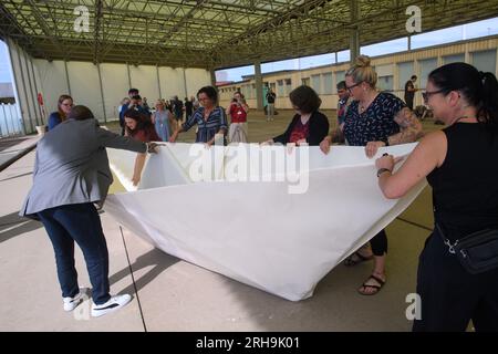 Marienborn, Deutschland. 15. Aug. 2023. Teilnehmer der Aktion „100 Boote - 100 Millionen Menschen“ falten ein riesiges Papierboot am German Division Memorial Marienborn. Die Papierbootfaltung war der Anstoß für ein deutschlandweites sozial kritisches Kunstprojekt der AWO Volunteer Academy Sachsen-Anhalt. Insgesamt müssen 100 große Papierboote an verschiedenen Stellen gefaltet werden. Die Kunstwerke werden in Berlin zum Weltflüchtlingstag am 20. Juni 2024 errichtet. Kredit: Klaus-Dietmar Gabbert/dpa/Alamy Live News Stockfoto