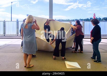 Marienborn, Deutschland. 15. Aug. 2023. Teilnehmer der Aktion „100 Boote - 100 Millionen Menschen“ falten ein XXL-Papierboot am German Division Memorial Marienborn. Die Papierbootfaltung war der Anstoß für ein deutschlandweites sozial kritisches Kunstprojekt der AWO Volunteer Academy Sachsen-Anhalt. Insgesamt müssen 100 XXL-Papierboote an verschiedenen Stellen gefaltet werden. Die Kunstwerke werden in Berlin zum Weltflüchtlingstag am 20. Juni 2024 aufgestellt. Kredit: Klaus-Dietmar Gabbert/dpa/Alamy Live News Stockfoto