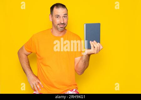Bärtiger hispanischer Mann in seinen 40ern, der der Kamera ein Buch zeigt, das bereichernde Gewohnheiten erzeugt, isoliert auf gelbem Studiohintergrund. Stockfoto