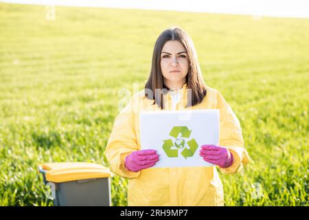 Person in Overalls hält Papier mit einem Anruf, um den Planeten zu retten, während sie auf dem grünen Feld bei Sonnenuntergang steht. Stockfoto