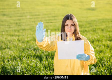 Die Person in Overalls hält Papier mit leerem Blatt Papier zur Textbeschriftung, während sie auf grünem Feld bei Sonnenuntergang steht, und die andere Hand zeigt eine Geste Stockfoto