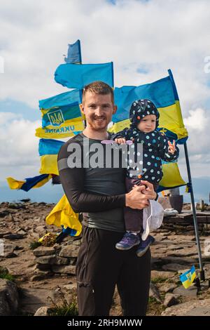 Ein Mann mit einem Baby auf dem Berg in der Nähe der ukrainischen Flaggen Stockfoto