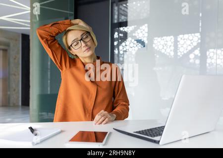 Geschäftsfrau müde am Arbeitsplatz, lange sitzende Arbeit im Büro, kranke Frau hat starke Nackenschmerzen, arbeitet am Laptop, während sie sitzt. Stockfoto