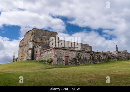 Blick auf die Ruinen des gotischen Friedhofs in der kantabrischen Stadt Comillas, mit einer grünen Wiese und blauem Himmel mit Wolken. Stockfoto