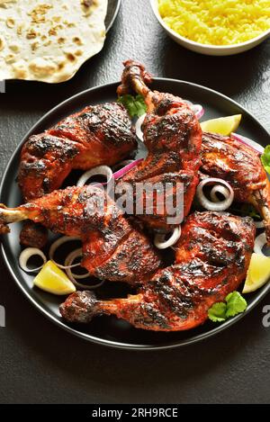 Tandoori-Hühnchen im indischen Stil auf dem Teller mit dunklem Steinhintergrund. Hähnchenschenkel mariniert in Joghurt und Gewürzen. Nahaufnahme Stockfoto