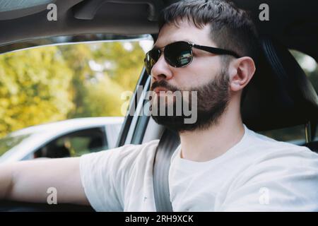 weißer Mann mit Bart in Sonnenbrille, der Auto fährt. Nahaufnahme Porträt Stockfoto