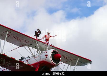 AeroSuperBatics Wingwalking-Team fliegt bei einer Flugshow. Wingwalker Stella Guilding auf einem Boeing Stearman Doppeldecker, gesponsert von Guinot. Mädchen auf dem Flügel Stockfoto