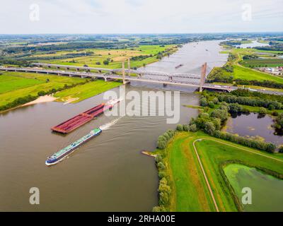 Hochwinkel-Drohnen-Point of View auf Frachtschiffen, die am Sommertag auf dem Waal River in Zaltbommel, Gelderland, Niederlande segeln Stockfoto