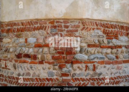 Strukturierte, uralte, geschwungene Wand aus Farbtönen und roten Ziegeln mit Fischgrätenmuster und verputztem Oberteil, Hintergrund mit Kopierbereich Stockfoto