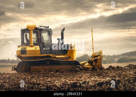 Radlader auf dem Feld eines Landwirts bei der Arbeit mit düsterem Himmel und Sonnenstrahlen Stockfoto
