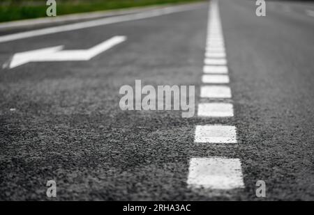 Fahrbahnmarkierungen. Tiefe der Bildaufnahme mit Fokus auf Asphalt nahe der Kamera. Straße mit zusätzlicher Fahrspur zum Abbiegen nach rechts. Stockfoto