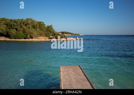 Wooden Pier with Ksamil Island during Sunny Day in Southern Albania. Beautiful Blue Ionian Sea with Landscape in Summer. Stock Photo