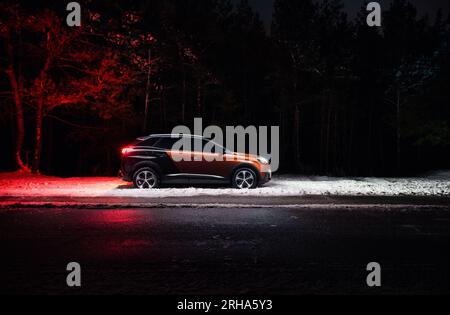 Seitenansicht der Peugeot 3008 GT-Linie im Nachtwald. Zweifarbiger Geländewagen parkt am Straßenrand im Winterwald, hinten sind Baumsilhouetten sichtbar Stockfoto