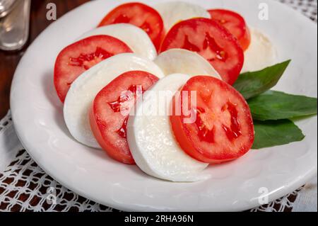 Itaianische vegetarische Speisen, frischer Caprese-Salat mit weißem, weichem italienischen Mozzarella-Käse, rote Tomaten und grünes Basilikum mit Olivenöl. Stockfoto