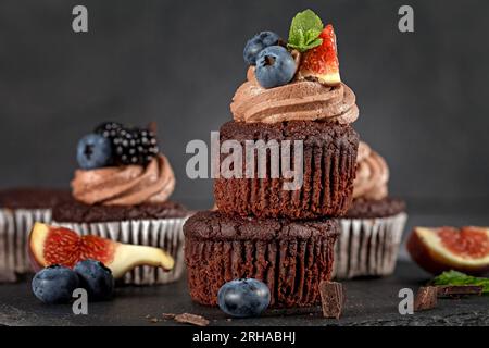 Schokoladen-Cupcakes. Heidelbeerfeige. Muffin mit Creme, Heidelbeere, Feige und frischer Minze auf dunklem Hintergrund Stockfoto
