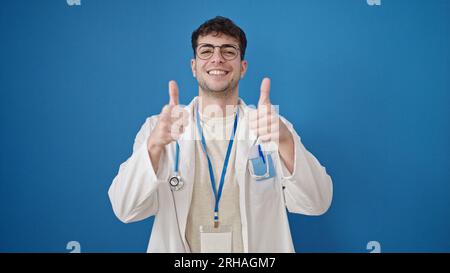 Junger hispanischer Arzt, der Daumen hoch über isoliertem blauem Hintergrund macht Stockfoto