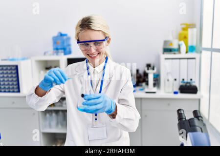 Junge blonde Wissenschaftlerin, die im Labor Flüssigkeit auf das Reagenzglas gießt Stockfoto