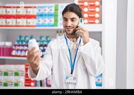 Junger hispanic Mann Apotheker hält Pillen Flasche reden auf dem Smartphone in der Apotheke Stockfoto